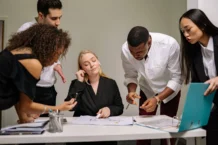 group of people standing beside the woman sitting at the desk